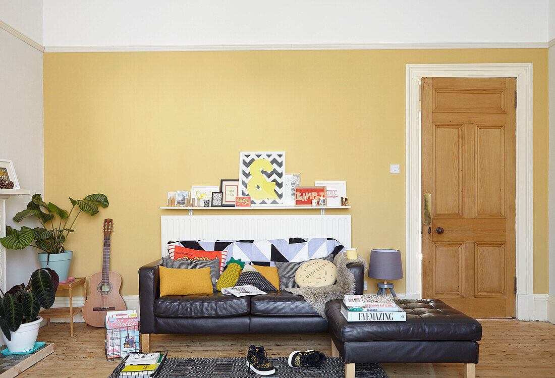 Schwarzes Ledersofa mit verschiedenen Kissen im gelben Wohnzimmer eines Hauses in Alloa, Schottland UK
