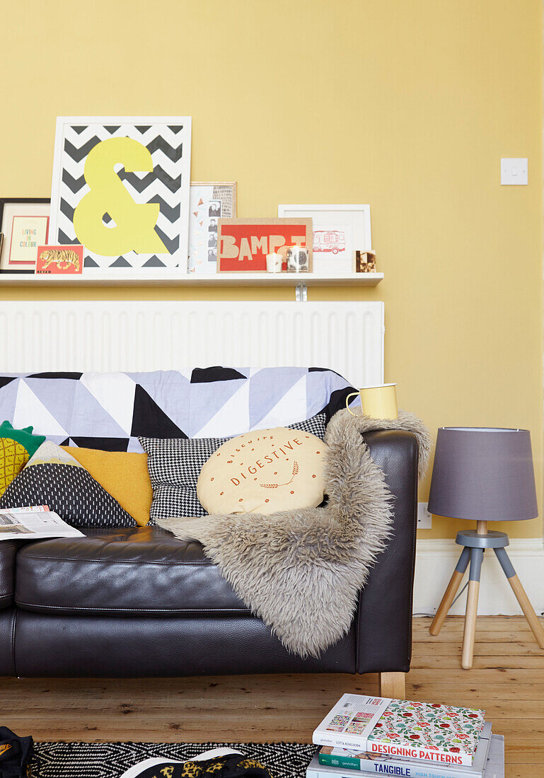 Verschiedene Kissen auf schwarzem Ledersofa im gelben Wohnzimmer eines Hauses in Alloa, Schottland UK