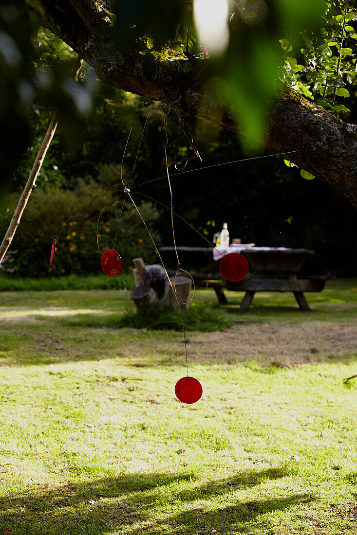 Red disc mobile and picnic table in Brabourne garden,  Kent,  UK