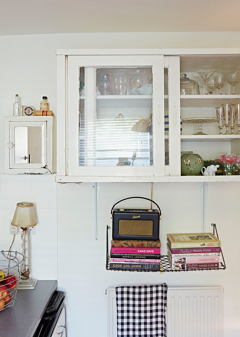 Radio und Bücher unter einer Glasvitrine in der Küche von Faversham, Kent, UK