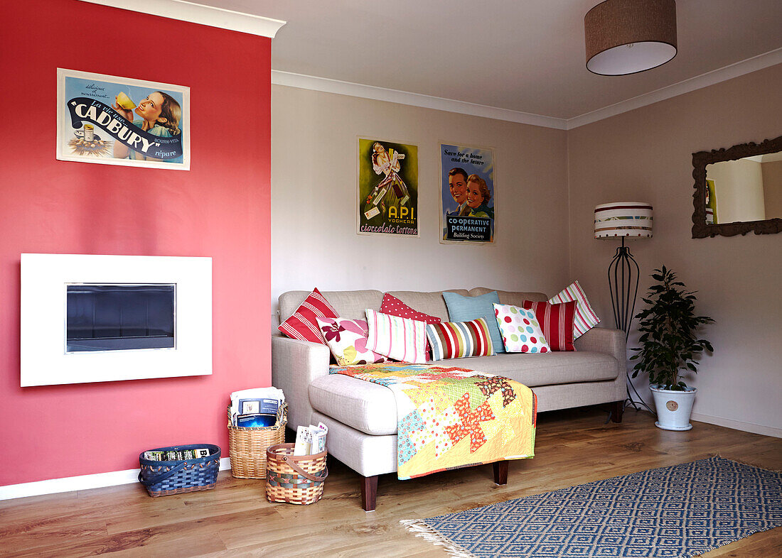 Rote Wand mit Print-Kollektion und bunten Kissen im Wohnzimmer eines Hauses in Bolton, Greater Manchester, England, UK