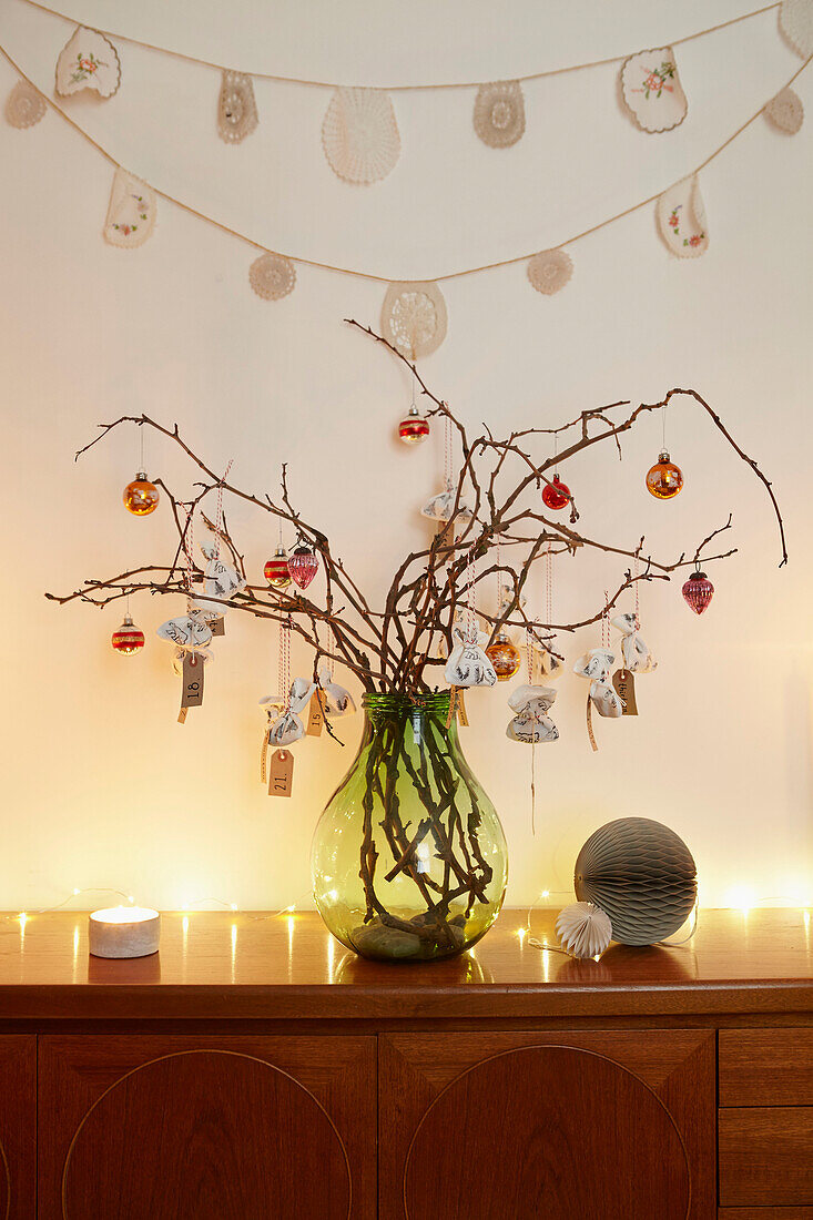 Weihnachtskugeln auf einem Zweig-Arrangement mit Beleuchtung auf einer Anrichte in einem Londoner Haus UK