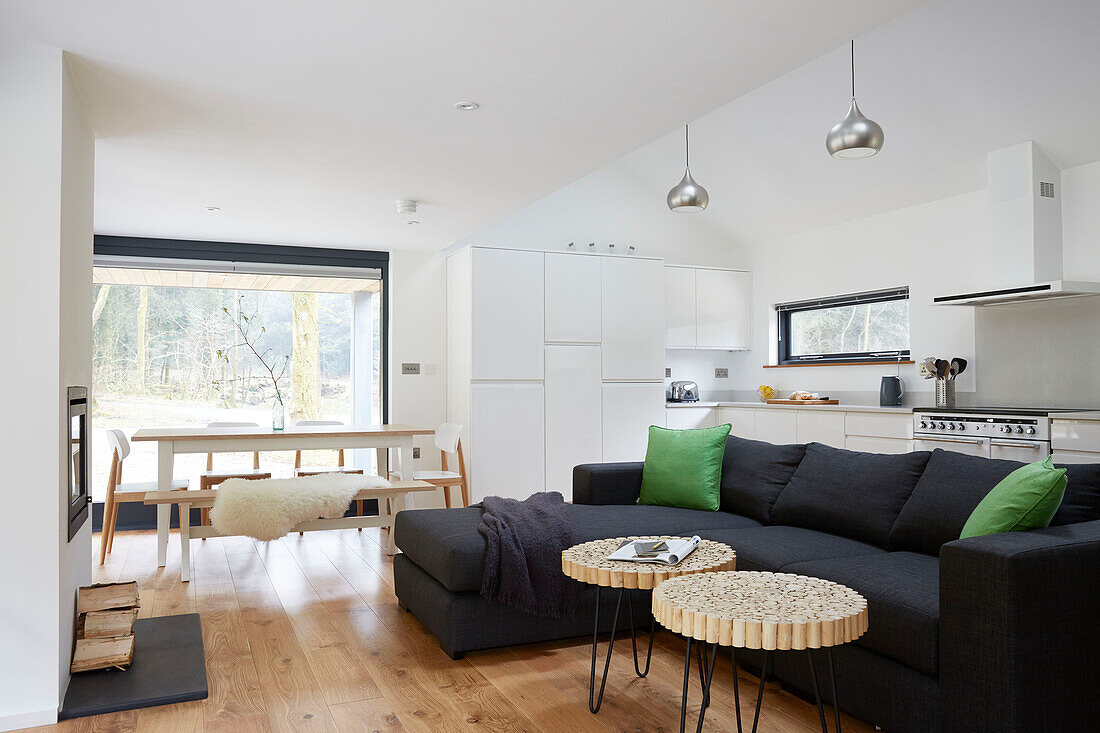 Black sofa with bright green cushions  and dining table with benches at window in Devon new build  UK