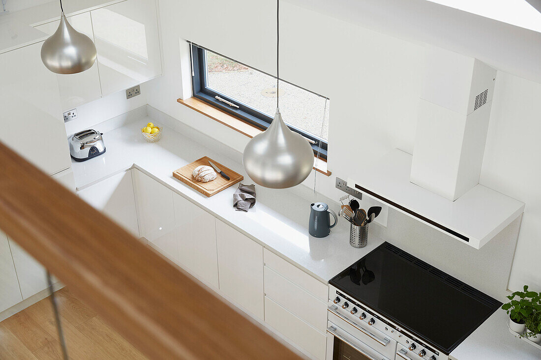 Blick auf die Küche mit silbernen Pendelleuchten im Zwischengeschoss eines Neubaus in Devon, Großbritannien