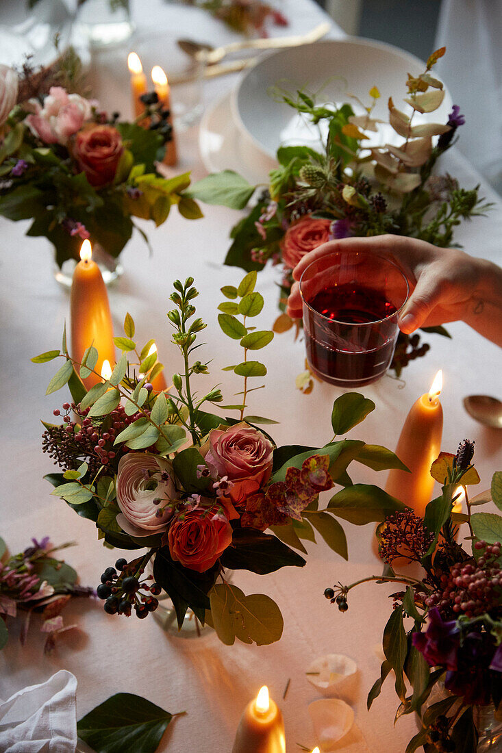 Hand hält Weinglas mit Blumenarrangements und brennenden Kerzen in einem Londoner Haus UK