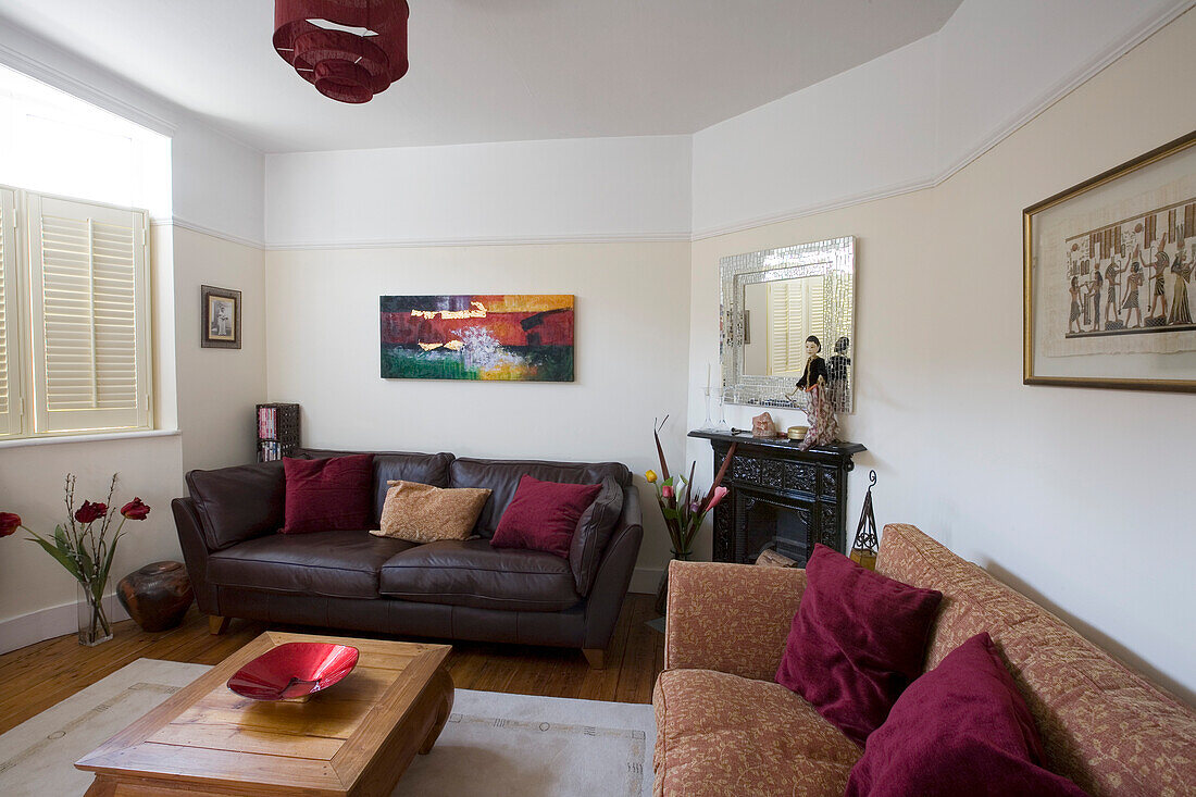 Artwork above brown leather sofa with wooden coffee table in living room of New Malden home, Surrey, England, UK