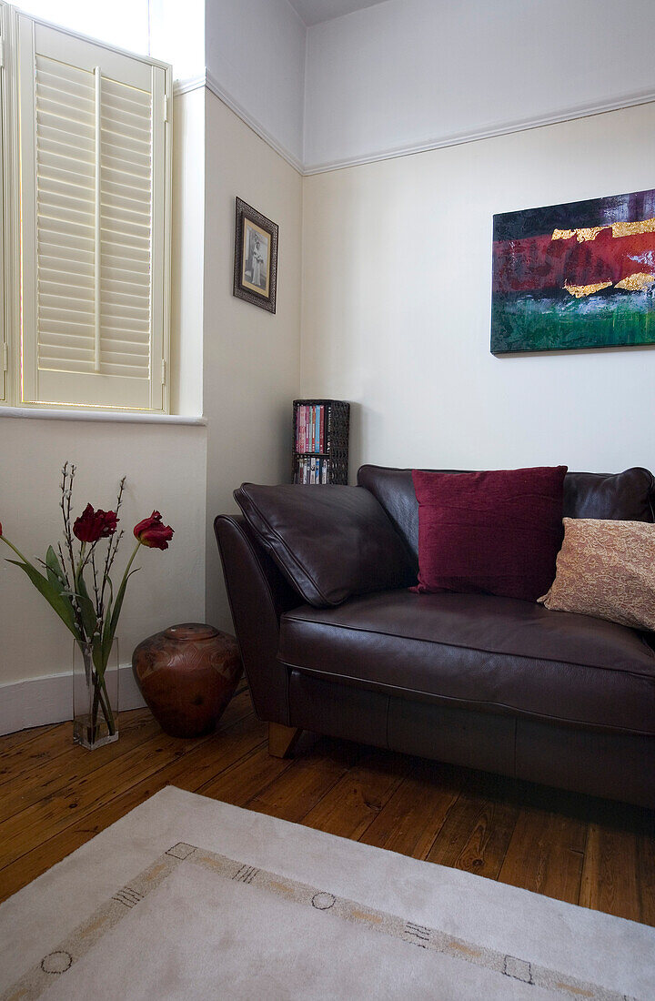 Artwork above brown leather sofa in New Malden home with shuttered window, Surrey, England, UK
