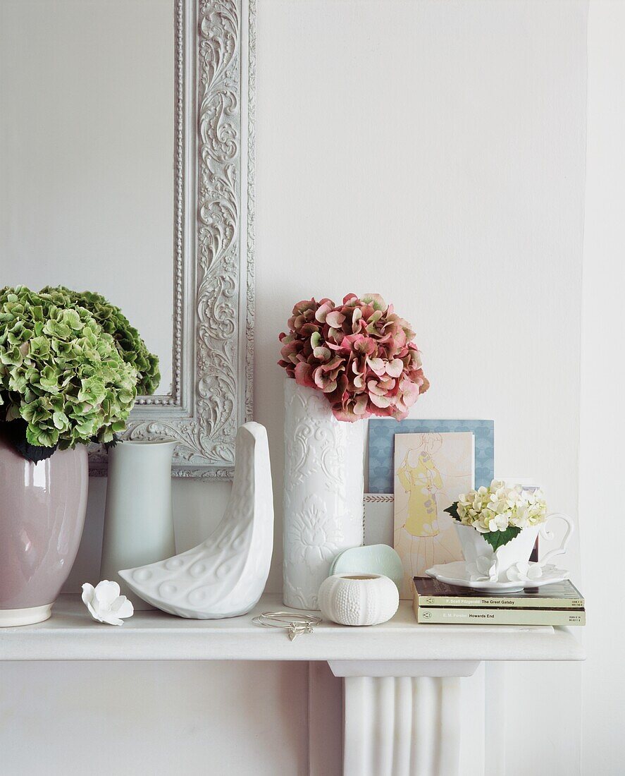 Detail eines weiß gestrichenen Kamins mit Vasen, Blumen und Geschirr sowie einem dekorativen Spiegel