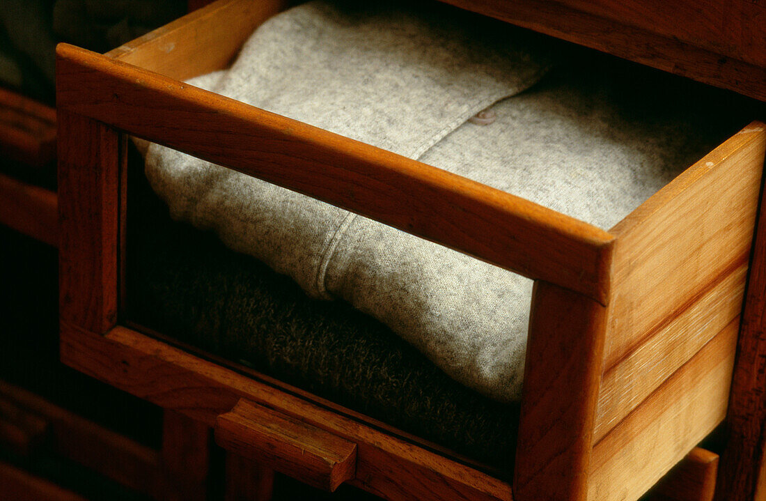 Detail einer offenen Holzschublade mit Sichtfenster und gefaltetem Pullover