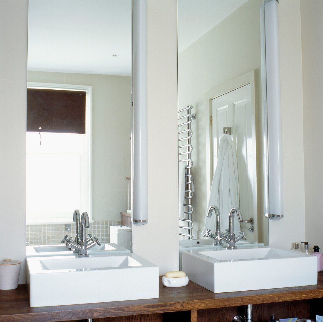 Nahaufnahme eines modernen Badezimmers mit zwei weißen Waschbecken in maßgefertigten Schränken aus dunklem Walnussholz vor langen Spiegeln
