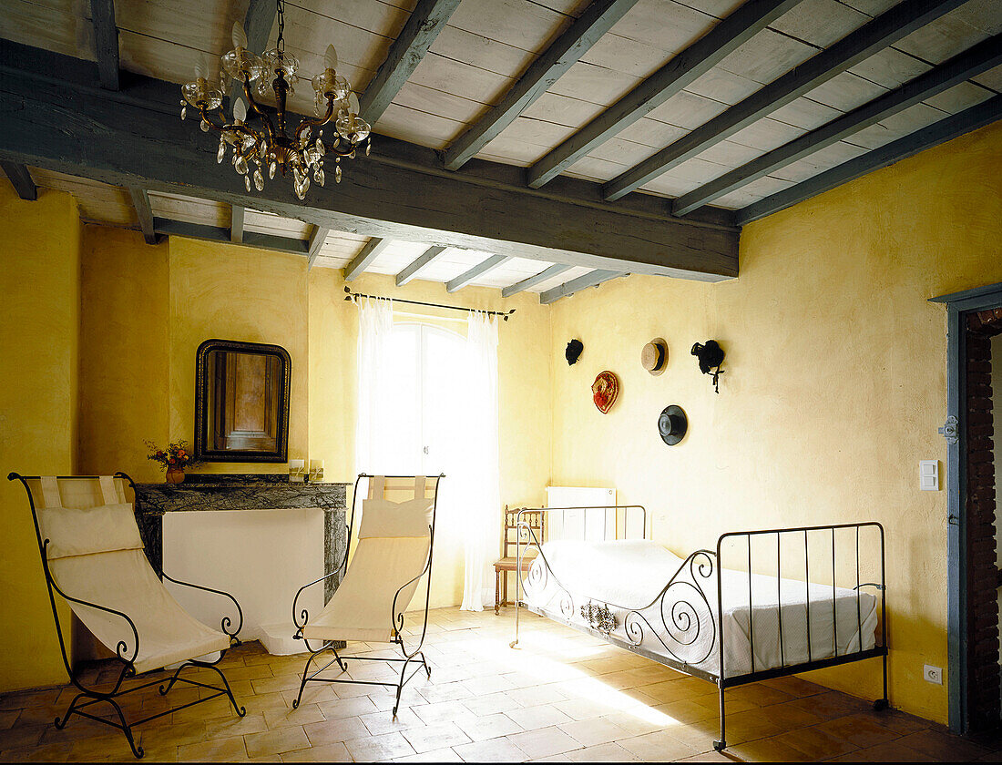 Traditionelles französisches Schlafzimmer in sonnigem Gelb und Pastellblau mit modernen dekorativen Eisenstühlen und Einzelbett