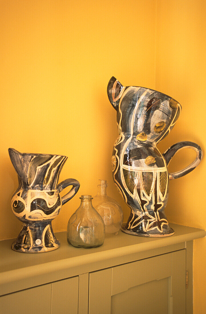 Studio pottery jugs against a yellow wall