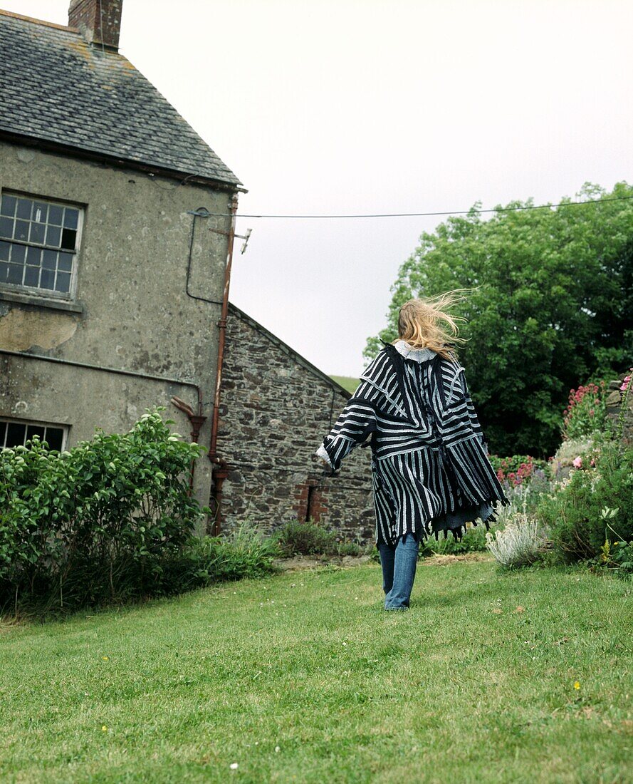 Frau in schwarz-weißem Filzmantel im Garten eines Bauernhauses