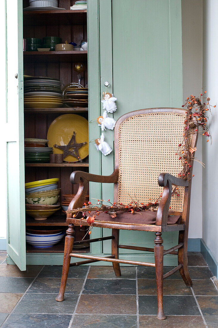 Can chair in kitchen corner with open cupboard door displaying tableware and crockery