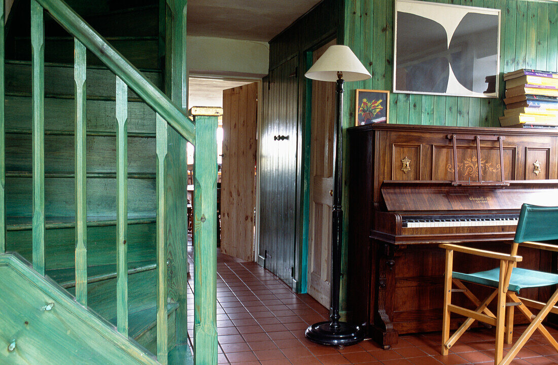 Staircase and boarded walls painted vibrant green wood stain in hallway with piano