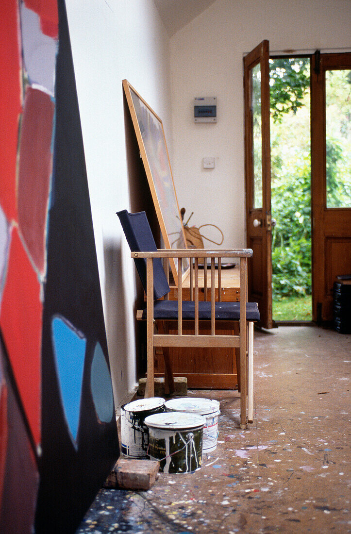 Tins of paint and canvas with chair in Suffolk artist's studio with open door