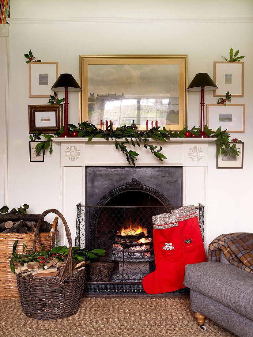 Open log fire with log basket and mantlepiece decorated with branches of bay and christmas stockings