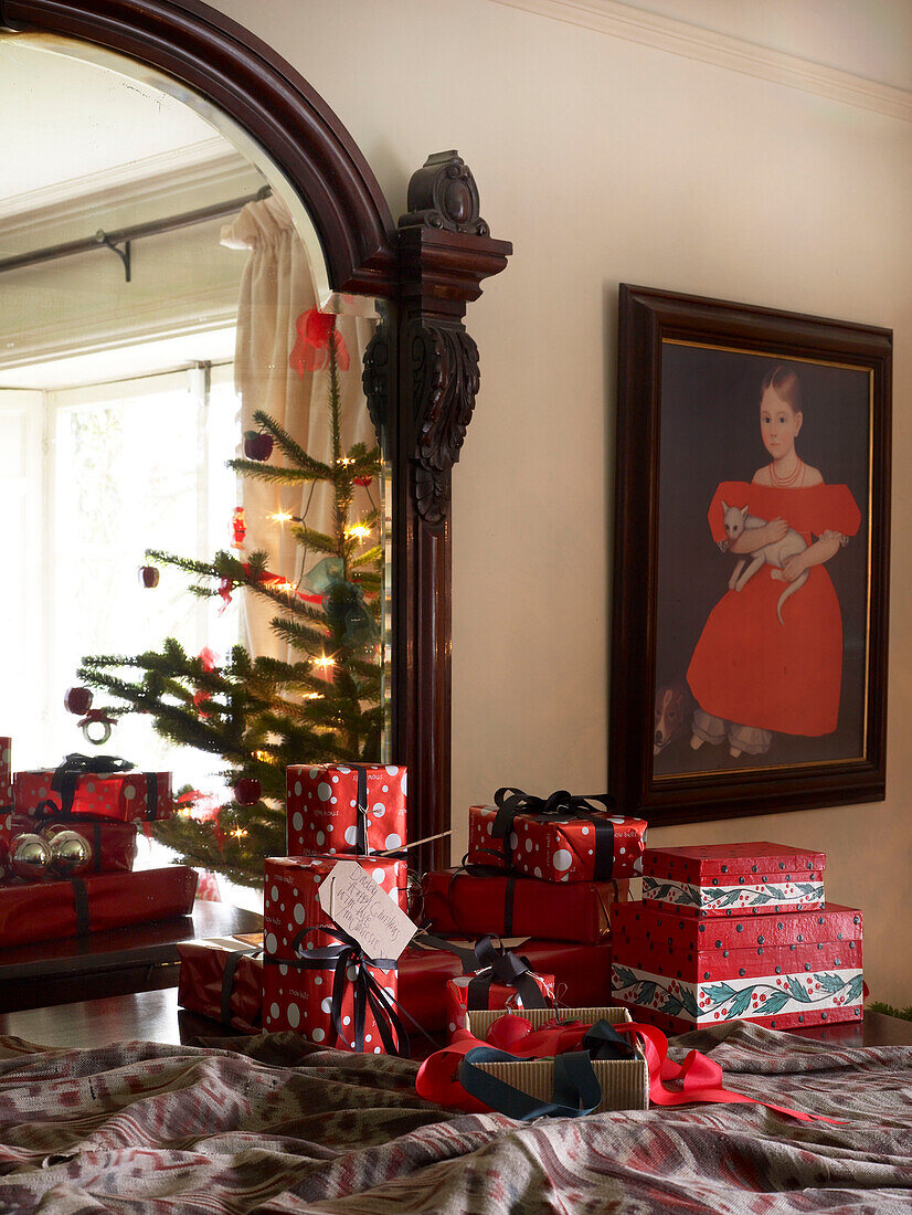 Reflexion eines geschmückten Weihnachtsbaums im Spiegel mit eingepackten Geschenken im Vordergrund