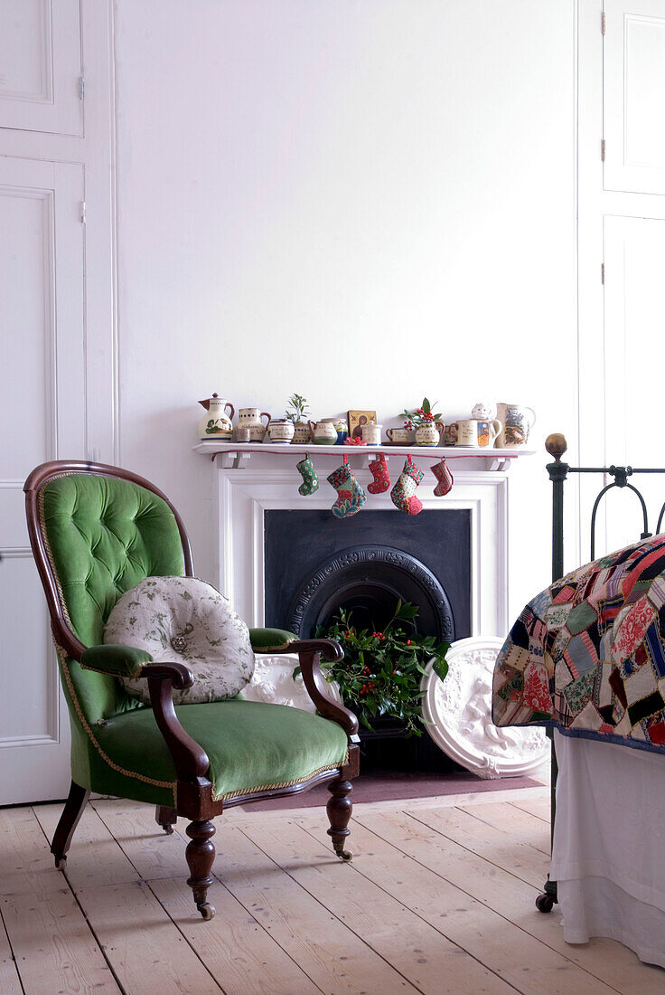 Bedroom detail with green velvet upholstered balloon back chair beside festive decorated fireplace