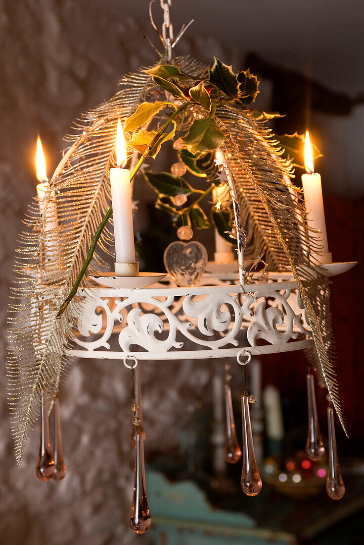Weißer Kronleuchter mit brennenden Kerzen, weihnachtlich geschmückt mit versilberten Federn, Stechpalmen und Glastropfen