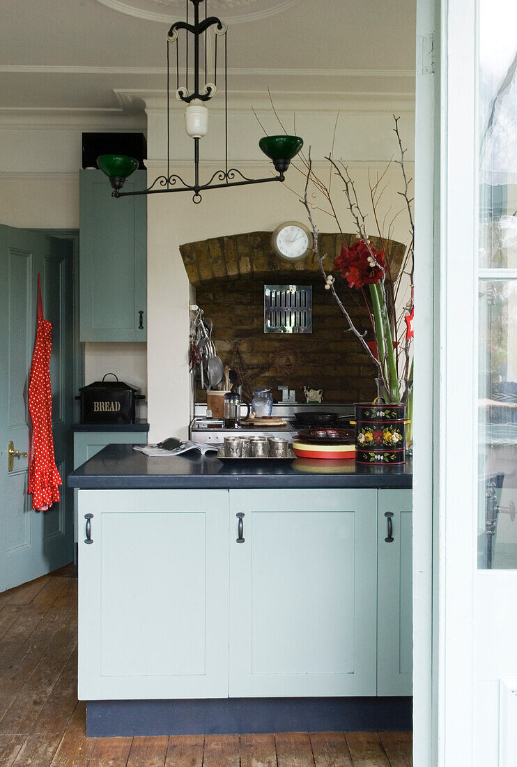 Gefleckte Schürze hängt an der Rückseite einer Küchentür mit freiliegendem Backstein-Kochfeld und pastellblauen Schränken