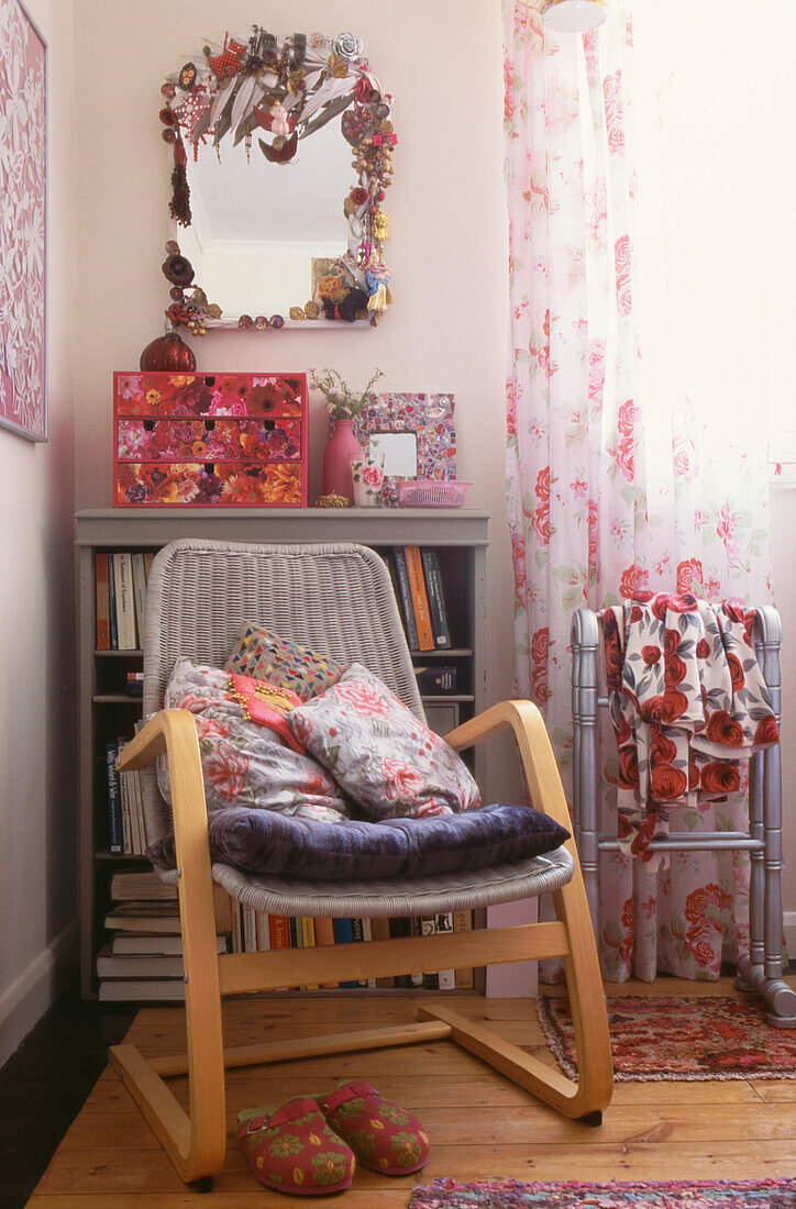 Can armchair with cushions in front of small bookcase and floral patterned curtains