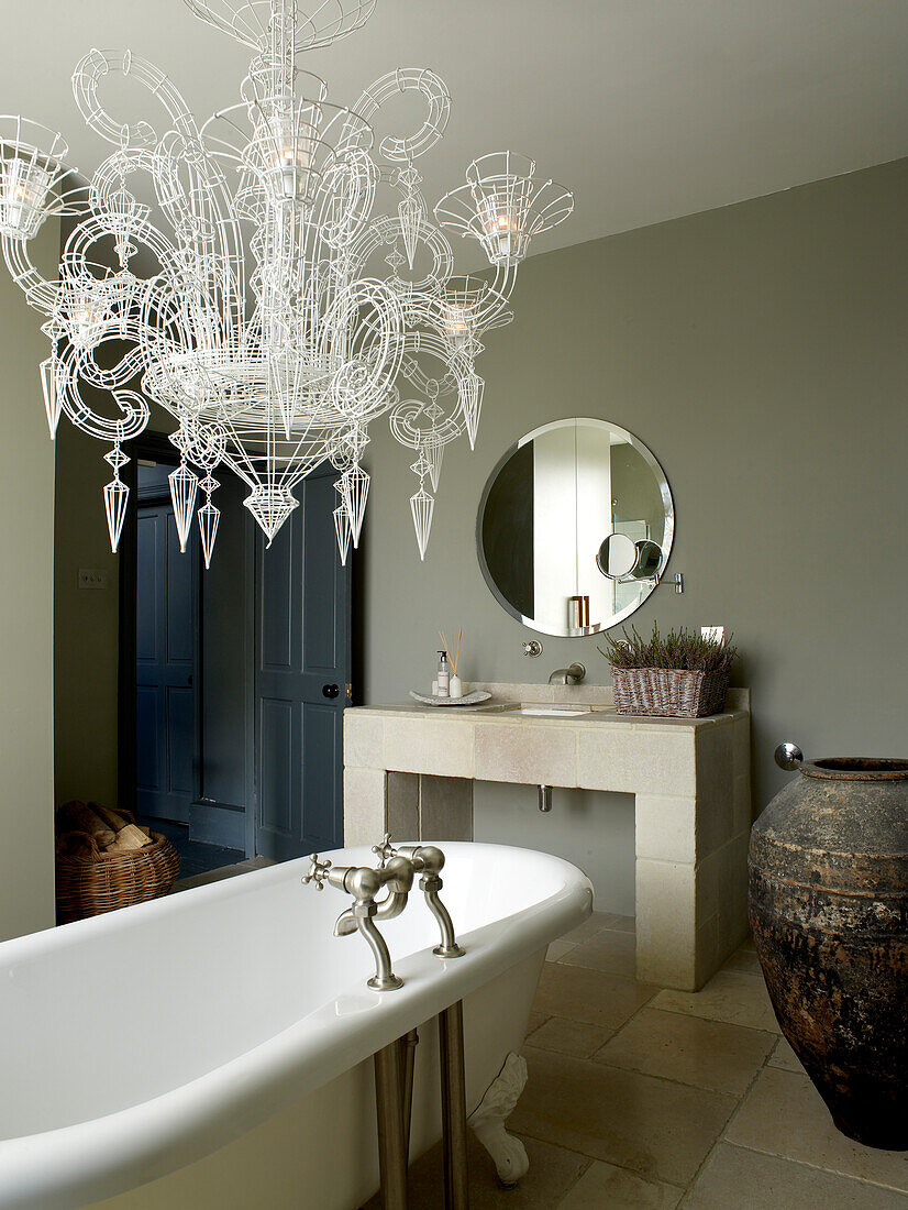 Neobarock-Kronleuchter aus Atelier-Drahtgeflecht über der Badewanne mit Rolltop in einem neutral grau und mit Stein gefliesten Badezimmer
