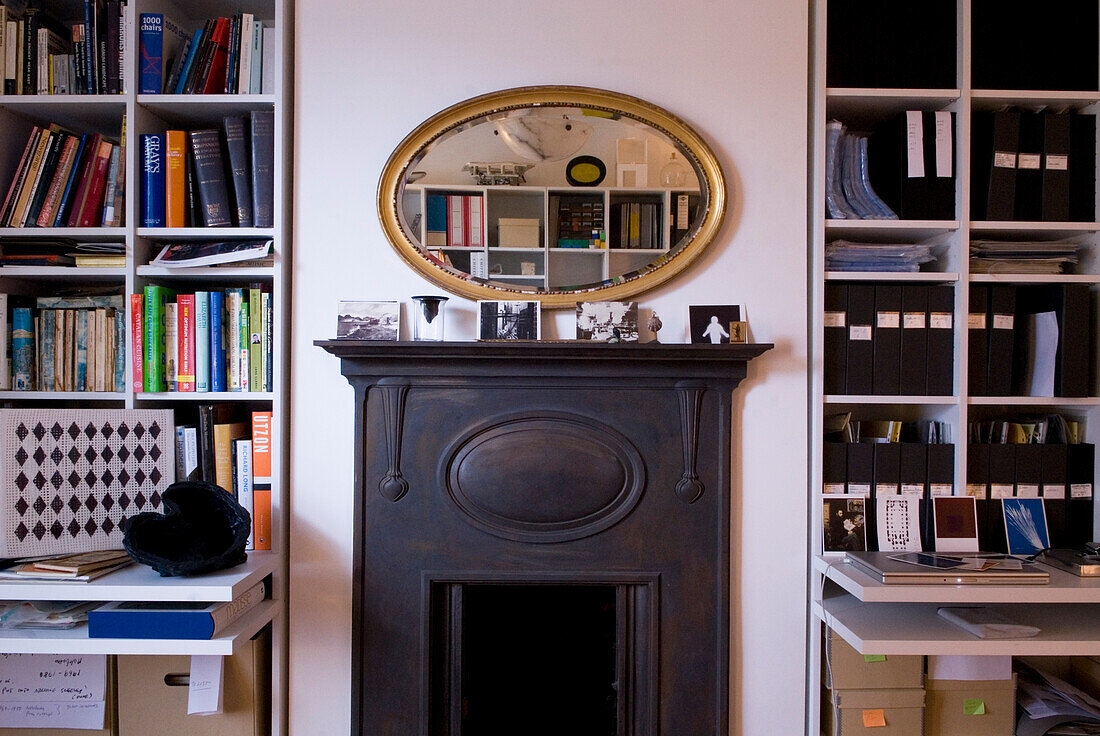 Oval mirror above fireplace with bookcases and filing