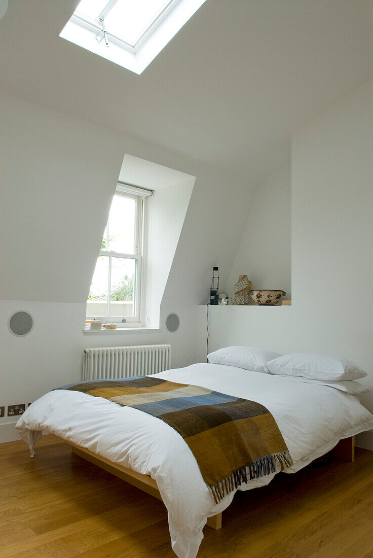 Doppelbett mit Decke in weißem Schlafzimmer mit Dachfenster