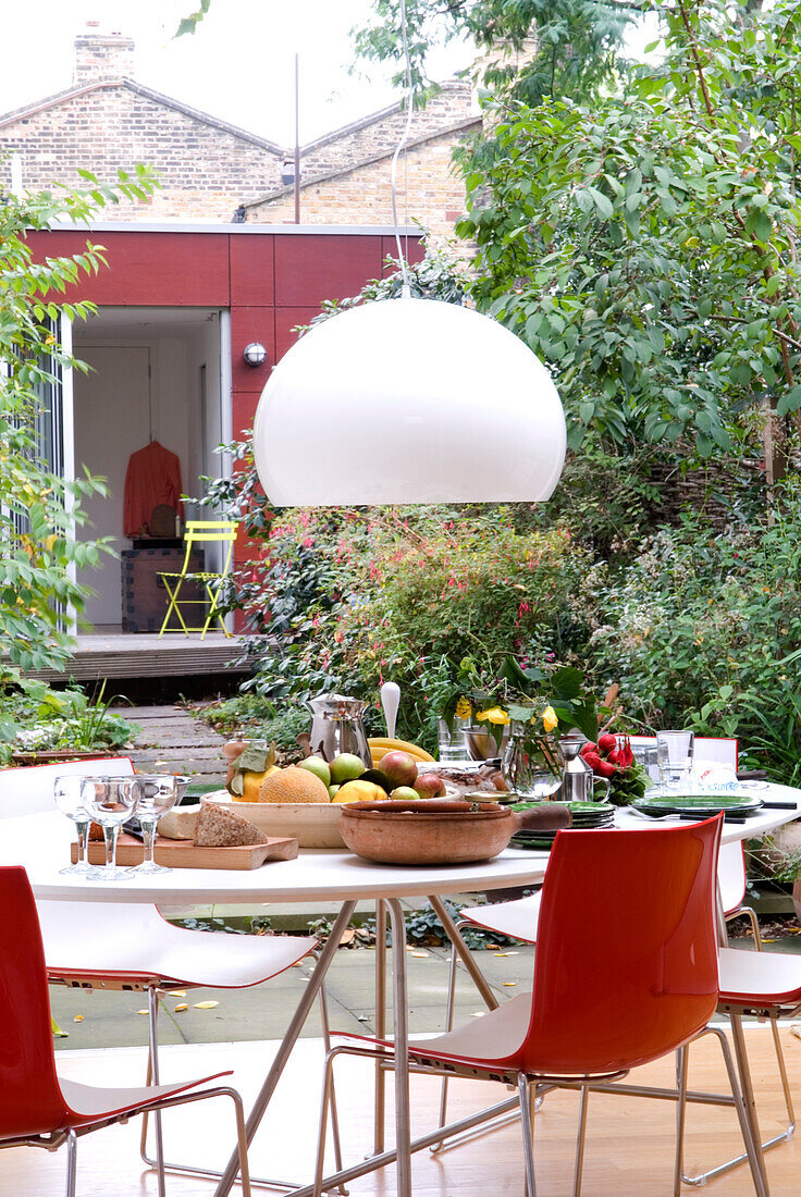 Weiße Pendelleuchte hängt über einem Gartentisch mit Obst und Brot