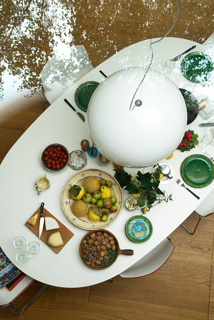 Blick auf eine weiße Hängelampe und einen mit grünem Geschirr gedeckten Esstisch