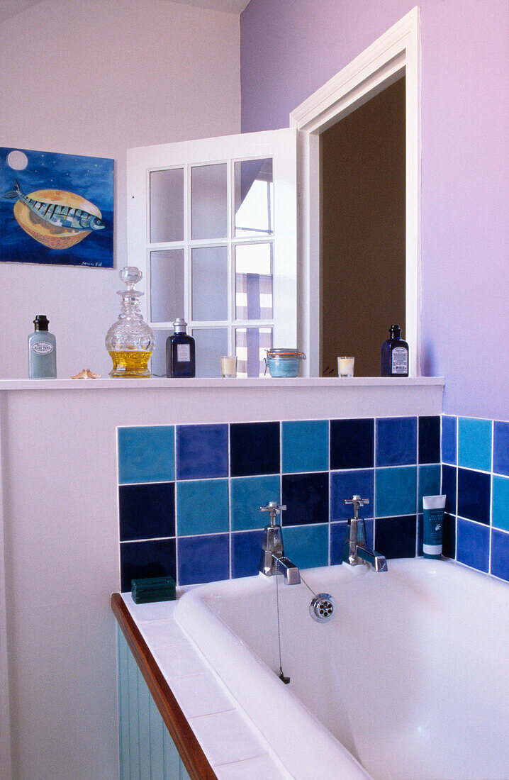 Lila und blaue Kacheln an der Badewannenverkleidung mit Toilettenartikeln auf einem Regal