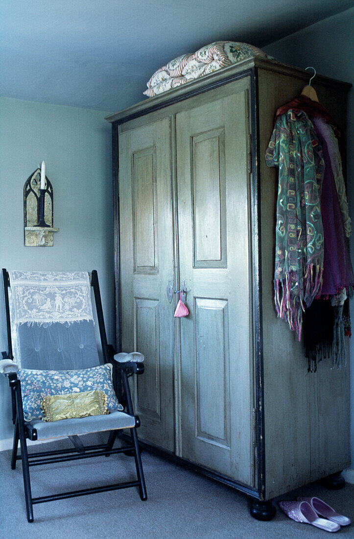 Wardrobe and folding chair in country bedroom with shawls