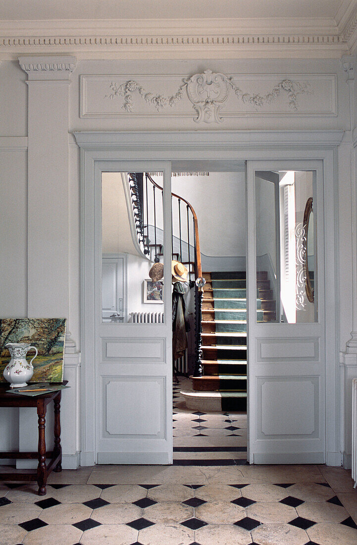Doppeltür mit Glasfüllung, die zu einer Treppe in einem gefliesten französischen Flur führt