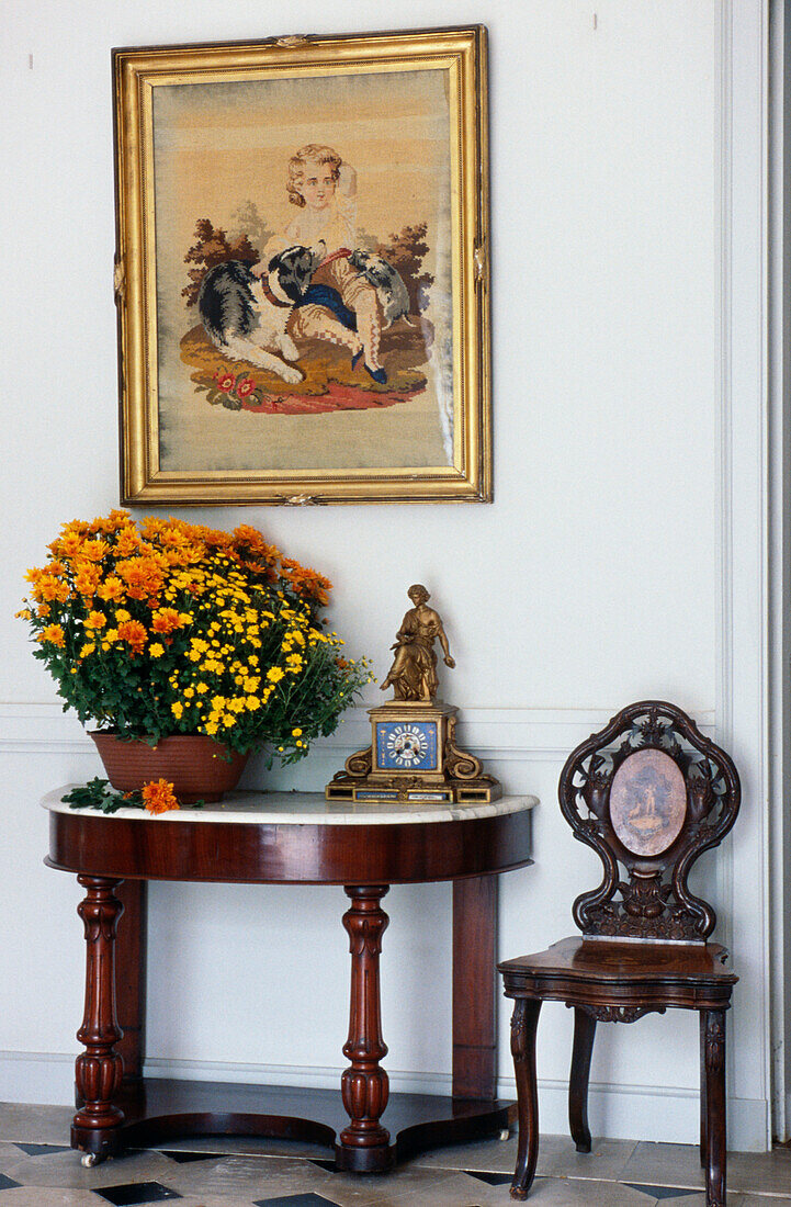 Orange houseplant on demilune in French hallway with artwork and chair