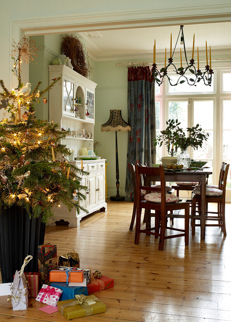 Christmas tree and presents in the open plan dining room with chandelier and table set for christmas