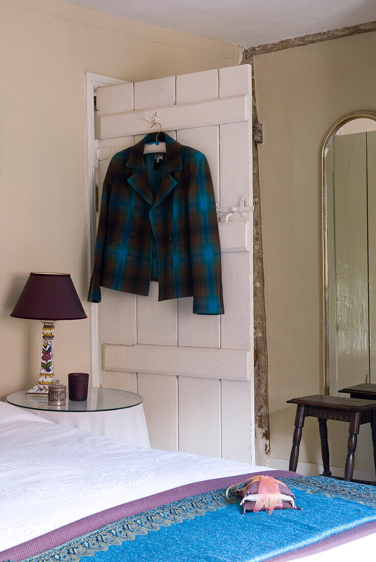 Detail des Bettes mit bestickter Bettwäsche und Decken und Jacke, die an der Rückseite einer Tür hängt