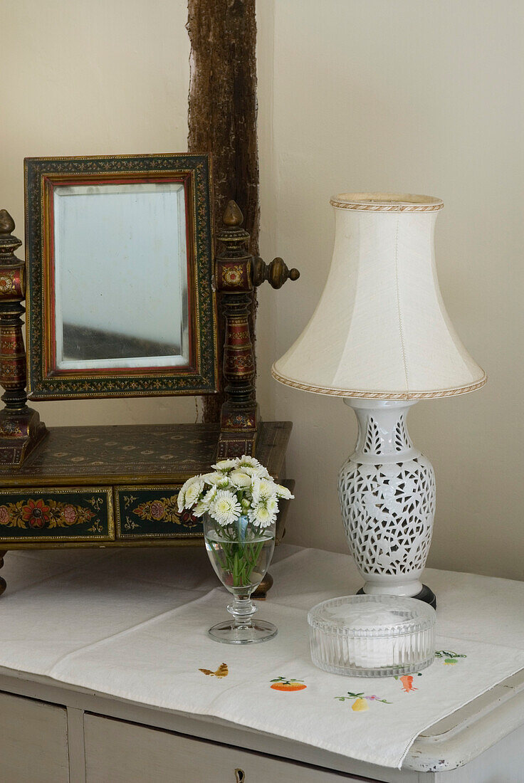 Dressing table detail with ornate mirror and lamp with glass of white flowers
