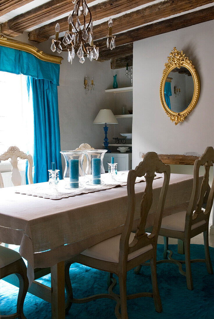 Esszimmer mit hellgrau gestrichenen Möbeln und seidenblauem Vorhang mit goldener Schabracke und blauem Teppich