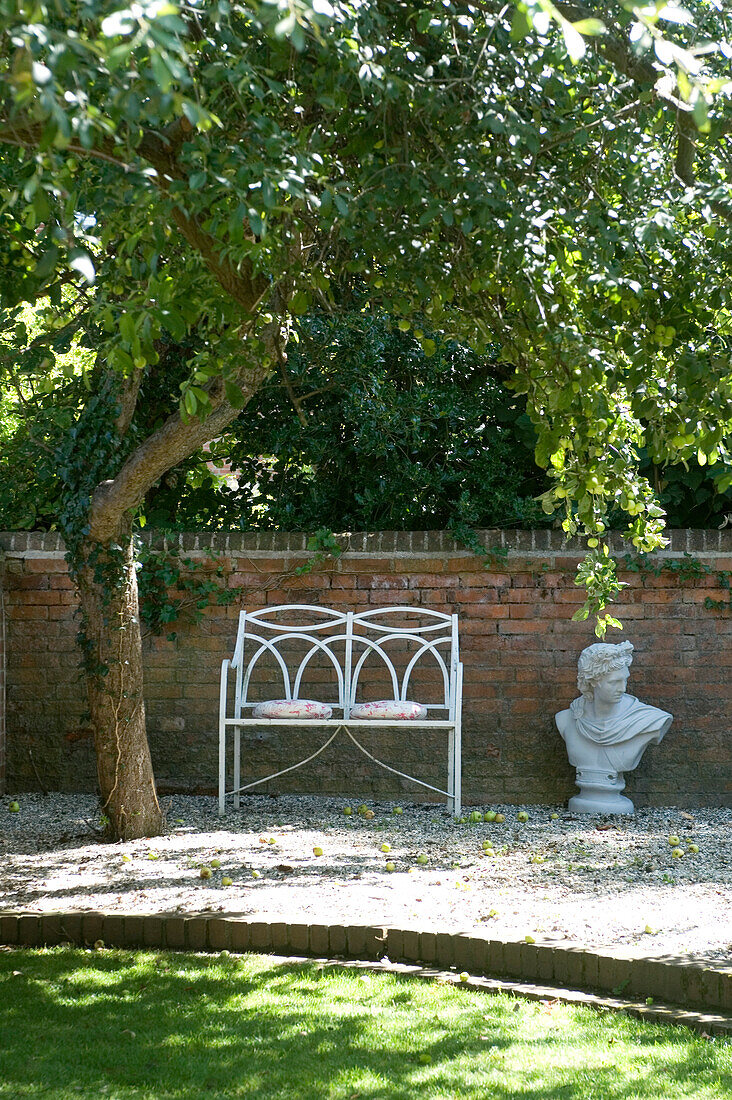 Kissen auf einem Metall-Gartensitz mit Büste in einem ummauerten Garten