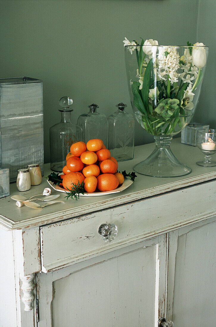 Blumengesteck in einer Glasvase und einem Stapel Orangen auf einem Schrank
