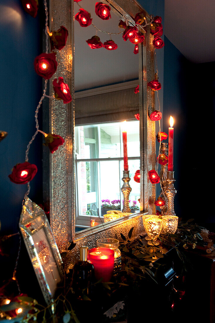 Lit candles and fairy lights on metal framed mirror in dark room