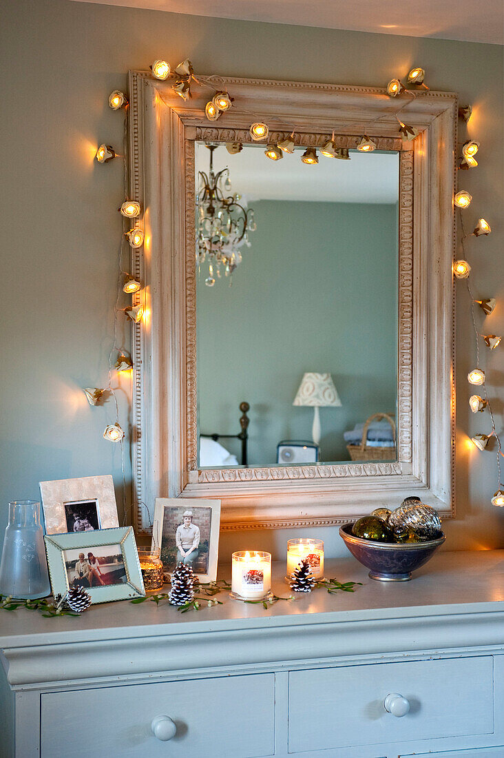 Familienfotos auf einer Kommode unter einem Spiegel mit beleuchteten Lichterketten