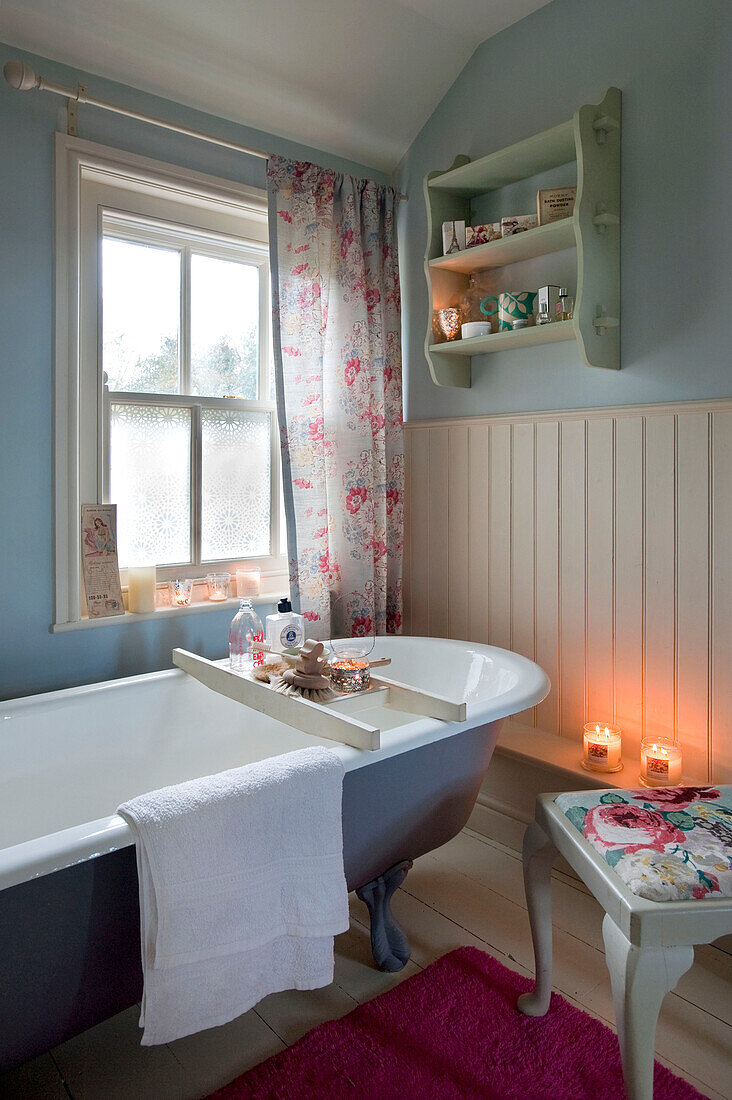 Freistehende Badewanne unter dem Fenster mit geblümten Vorhängen in einem getäfelten Badezimmer in Hereford