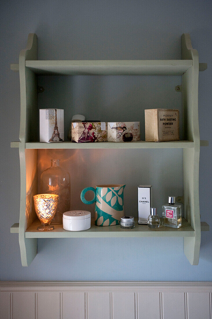 Perfumes and lit candles on wall mounted shelf unit