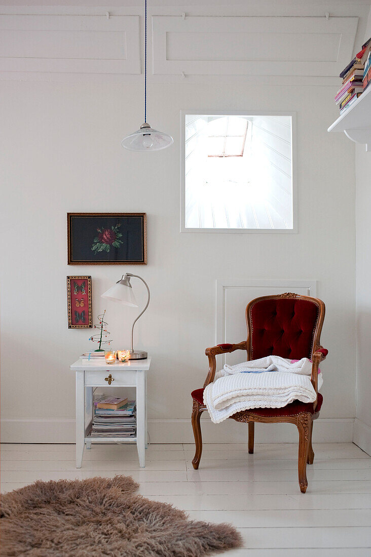 Armchair below square mirror with side table and embroidery in Odense bedroom