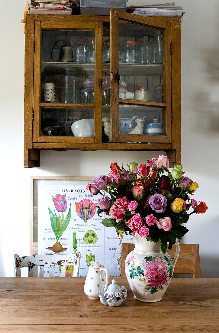 Kitchen table with glass wall mounted vintage cupboard and vase of cut flowers