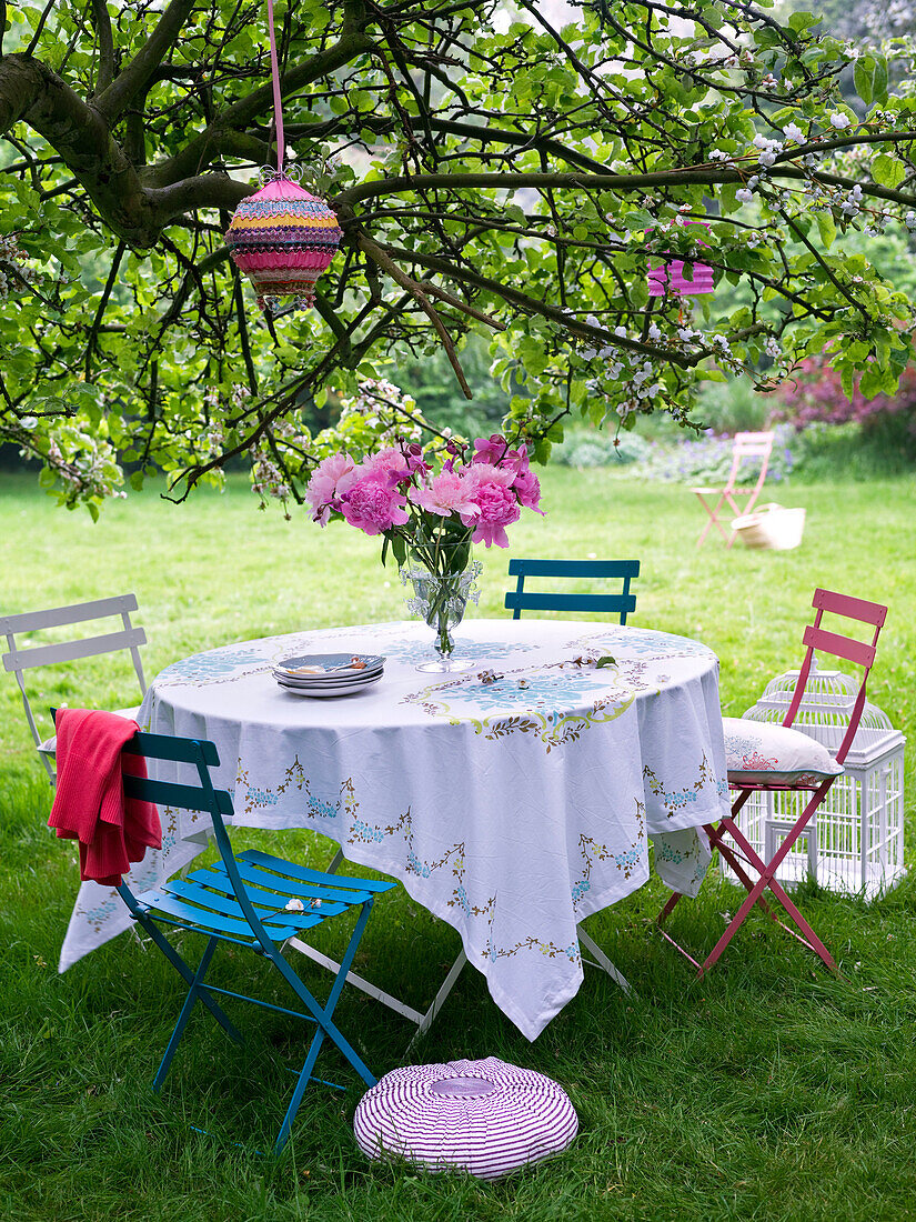 Sommerlicher Gartentisch unter einem Baum mit Papierlaternen, die in einem Baum hängen