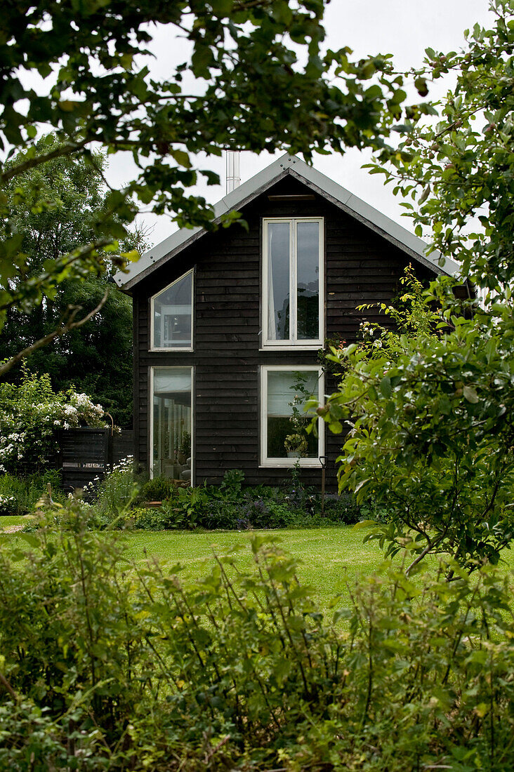 Außenansicht eines Hauses mit Holzverschalung in einem grünen Garten