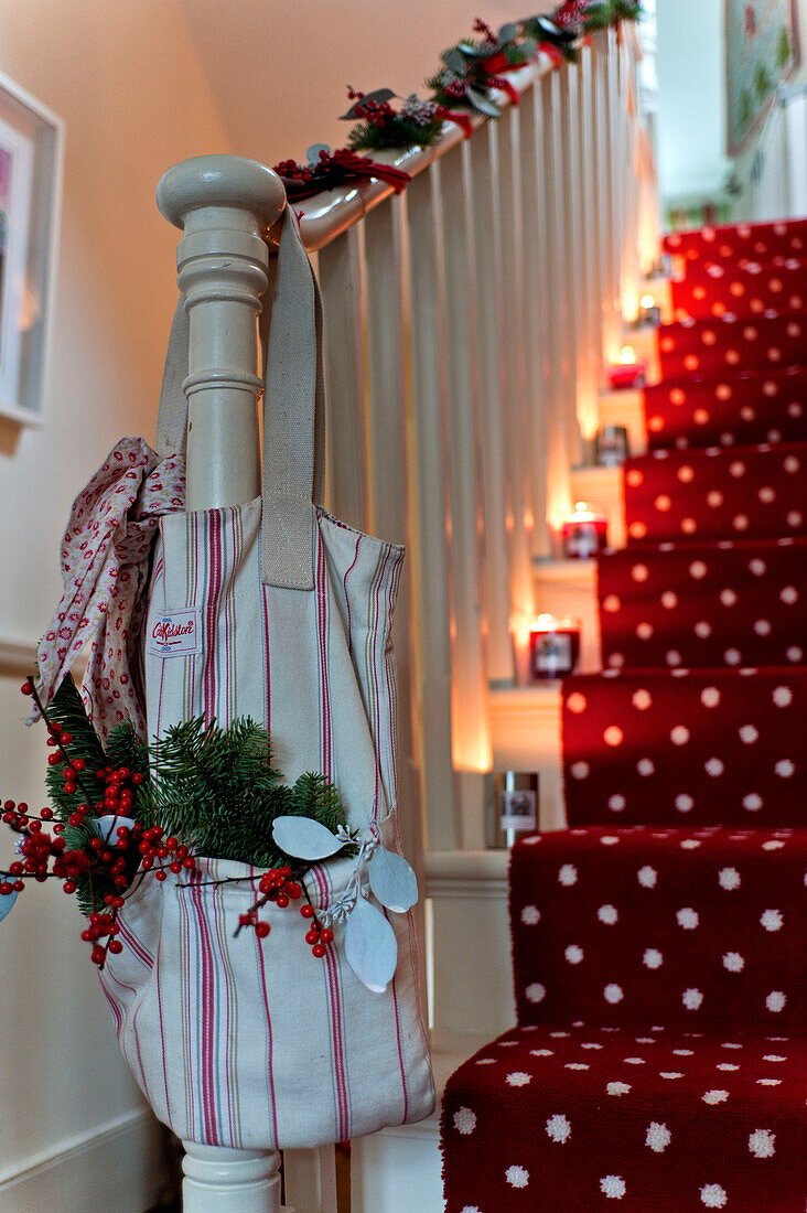 Weihnachtsdekoration in einer Tüte am Geländer einer kerzenbeleuchteten Treppe in einem Londoner Haus UK